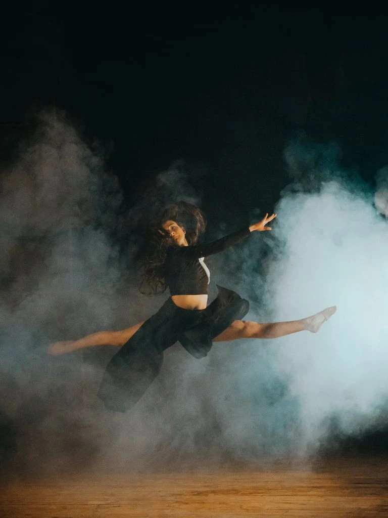 A dancer leaps through morning light in an empty rehearsal hall.
