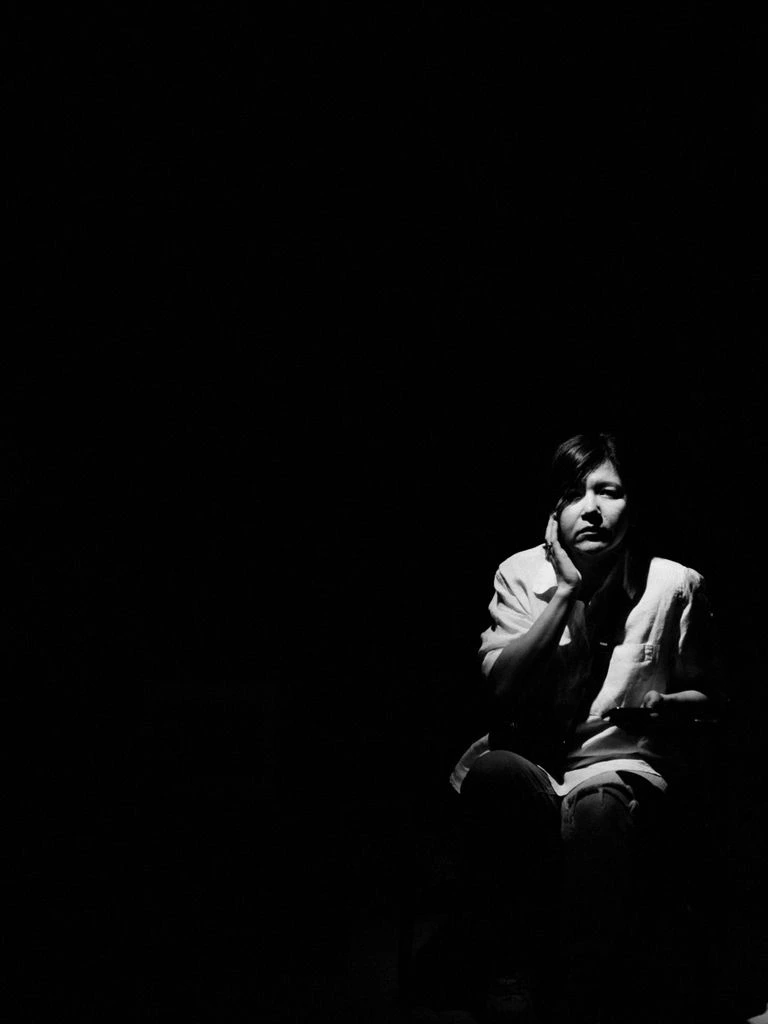 A solitary critic taking notes in a darkened cinema with the projector beam cutting through haze.
